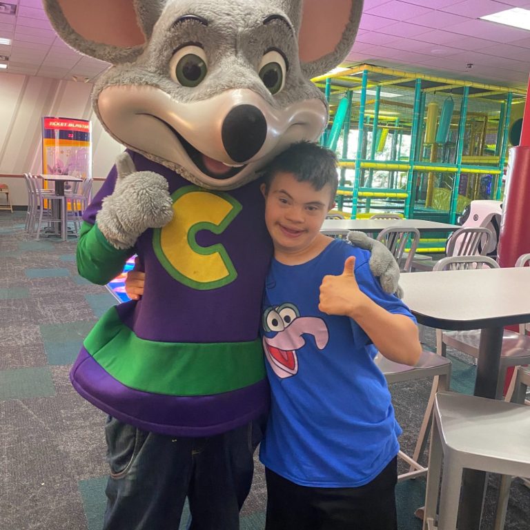 Boy standing besides a Chuck E. Cheese character found at the restaurant with the same name